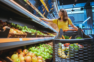 Wall Mural - woman taking apples from supermarket store shelf