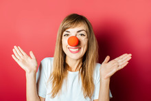 Young Beautiful Woman With A Red Nose Of A Clown On A Pink Background. Concept Red Nose Day, Holiday, Party, Clown