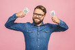 Happy winner with jackpot. Pleased bearded business man in casual holding money while looking at the camera isolated over pink background.