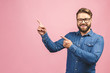 Surprised happy bearded man in shirt pointing away isolated over pink background.