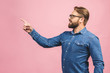 Surprised happy bearded man in shirt pointing away isolated over pink background.