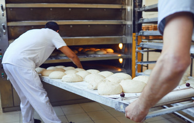 two bakers are pushing a tray of bread into the oven at the bakery