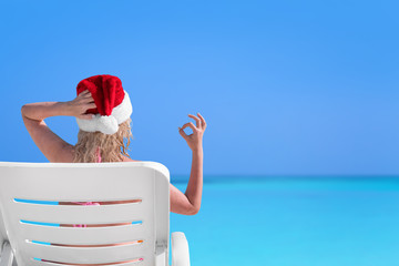 Wall Mural - Woman in Santa Claus Hat show gesture Okay on sunbed at beach with turquoise sea view