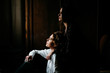 © Thais Ramos Varela/Stocksy - beautiful young lesbian couple looking through the window and smoking in a dark room