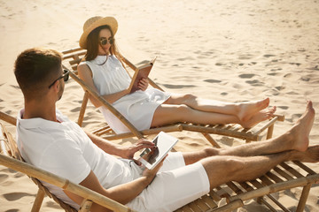 Wall Mural - Young couple relaxing in deck chairs on sandy beach