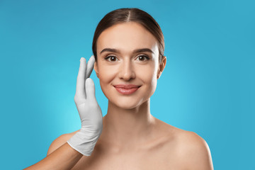 Poster - Doctor examining woman's face before plastic surgery on light blue background