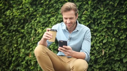 Wall Mural - happy young man take a sip of coffee while using his smart phone in the street