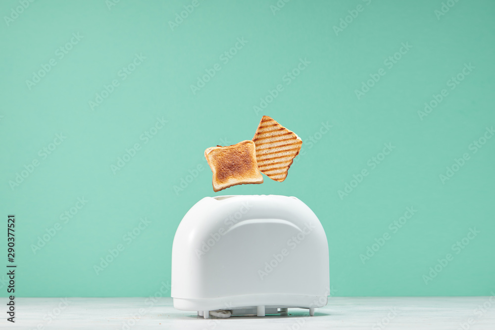 Roasted toast bread popping up of toaster with green wall, front view - obrazy, fototapety, plakaty 