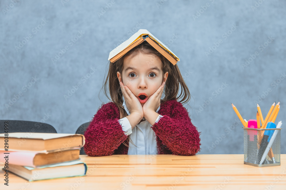 A cheerful girl sitting and holding a book over her head over a gray ...