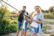 © Олег Кошевський - Happy young family fishing on the lake. They smile, hold fishing rods and fishnets in their hands. The little daughter helps her parents fish. Wonderful landscape of the lake at sunset