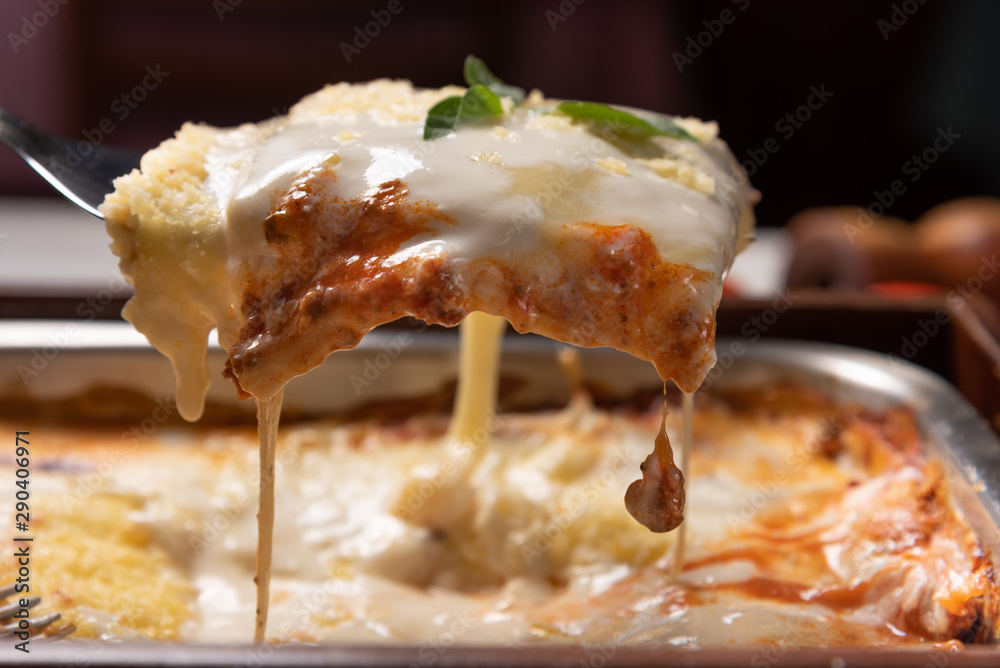 Delicious lasagna made with minced beef bolognese sauce and bechamel sauce topped with basil leaves, soft light - obrazy, fototapety, plakaty 