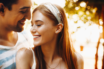 Wall Mural - Outdoor shoot of a lovely young couple smiling. Beautiful red haired woman laughing while embracing with her boyfriend.