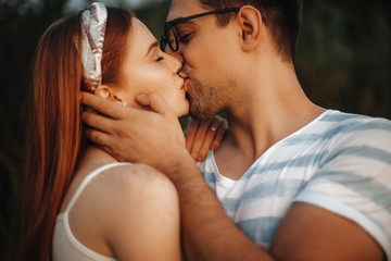 Wall Mural - Close up of a charming couple kissing with closed eyes while man is touching face of her girlfriend with hand outdoor while dating.