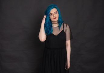 Wall Mural - People and fashion concept - Woman dressed in black dress and blue hair posing over black background