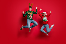 Full Size Photo Of Funky Lady And Guy Jumping Excited By X-mas Prices Wear Ugly Ornament Jumpers And Headwear Isolated Red Color Background