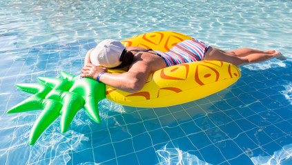 Wall Mural - Woman swimming in the pool on inflatable pineapple