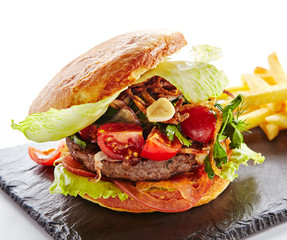 Canvas Print - Fresh Beef Burger with Bacon, Fried Onions, Tomato Sauce, Pickled Cucumbers, Green Lettuce, Cheese and French Fries Garnish. Hamburger or Beefburger on Natural Black Stone Plate Isolated on White