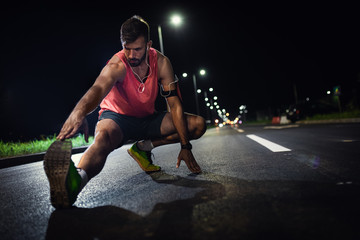 Wall Mural - Portrait of young fitness man standing on road preparing to run at night.