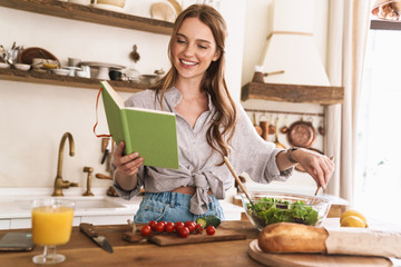 Pretty lady indoors at the kitchen cooking holding notebook.