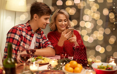 holidays, technology and celebration concept - happy couple having christmas dinner at home and usin