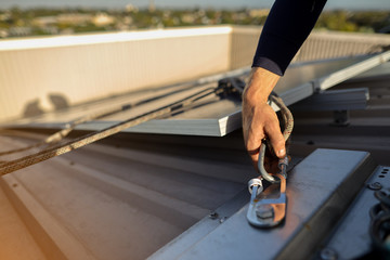 Wall Mural - Rope access technician inspector inspecting rigging rope and locking carabiner fixed into permanent abseiling roof anchor point construction building site prior to used, Sydney, Australia   