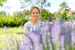 gardening and people concept - happy young woman sitting near lavender flowers on summer garden bed