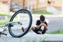 Kid Hurts His Leg After Falling Off His Bicycle. Child Is Learning To Ride A Bike. Boy In The Street Ground With A Knee Injury Screaming After Falling Off To His Bicycle.