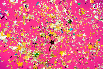 Wall Mural - Pink background on which a lot of multi-colored clapperboard foil and stars confetti, holiday concept. Christmas card. Place for text.