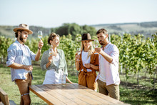 Group Of Young Friends Dressed Casually Having Fun Together, Tasting Wine On The Vineyard On A Sunny Summer Morning