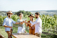 Group Of Young Friends Dressed Casually Having Fun Together, Tasting Wine On The Vineyard On A Sunny Summer Morning