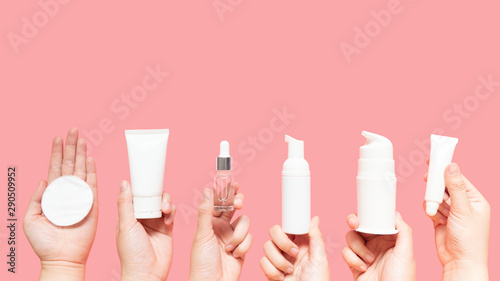 Cuadros en Lienzo Skincare routine step for healthy skin - Woman hands holding facial cotton pad, foam, essential oil, serum, lotion and eye cream packaging on pink background