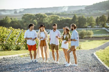 Wall Mural - Group of young friends dressed casually hanging out together, walking with wine glasses on the vineyard on a sunny day