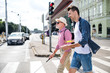 © Halfpoint - Young man and blind senior with white cane walking in city, crossing street.