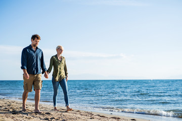 Wall Mural - Young couple walking outdoors on beach, holding hands. Copy space.