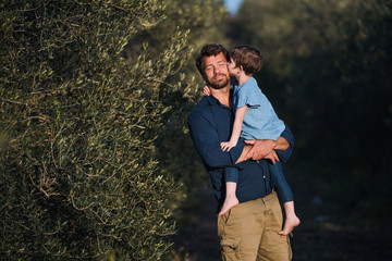 Wall Mural - Father with small daughter standing outdoors by olive tree, kissing.