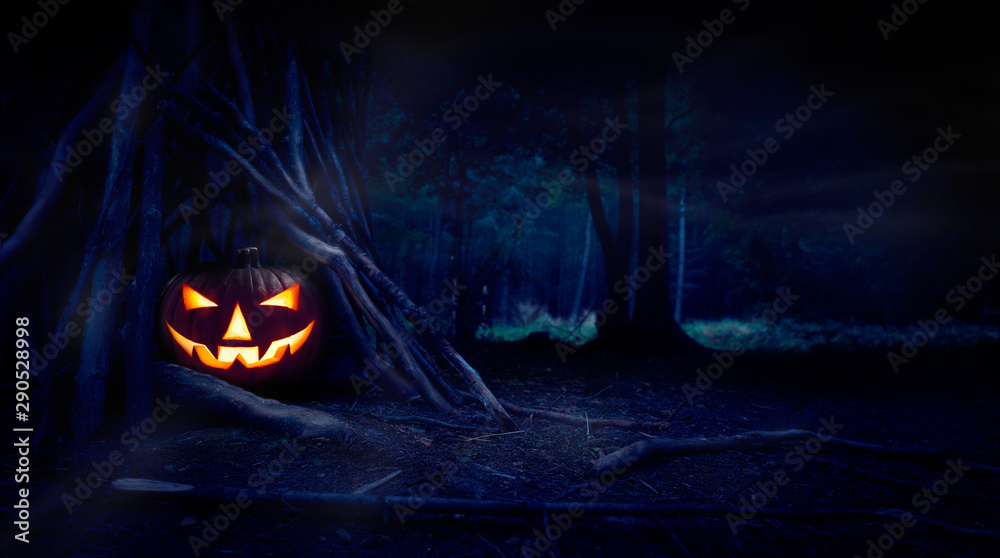 A single halloween Jack O Lantern hiding in a wood shelter, campsite on the forest floor on the left side of frame with space for text on the right. - obrazy, fototapety, plakaty 