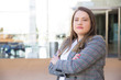 © Mangostar - Front view of confident young woman with crossed arms. Serious young manager standing near office building and looking at camera. Concept of confidence