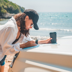 Wall Mural - woman checking map on car hood drinking coffee at summer sea beach