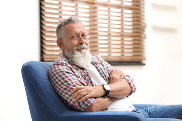 Wall Mural - Portrait of handsome mature man sitting in armchair indoors