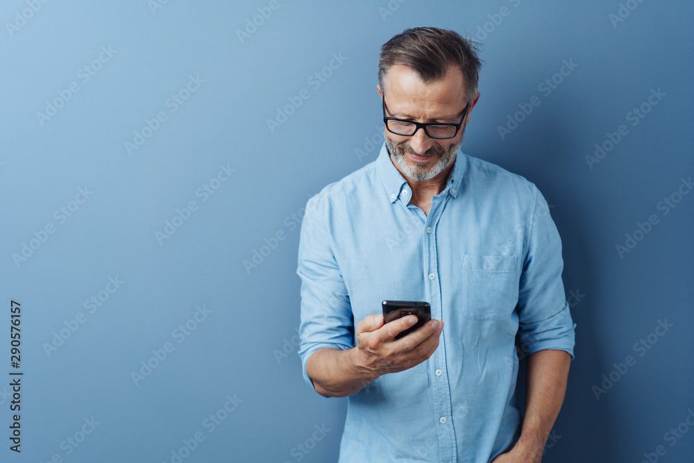 Man smiling as he reads a text message on a mobile - obrazy, fototapety, plakaty 