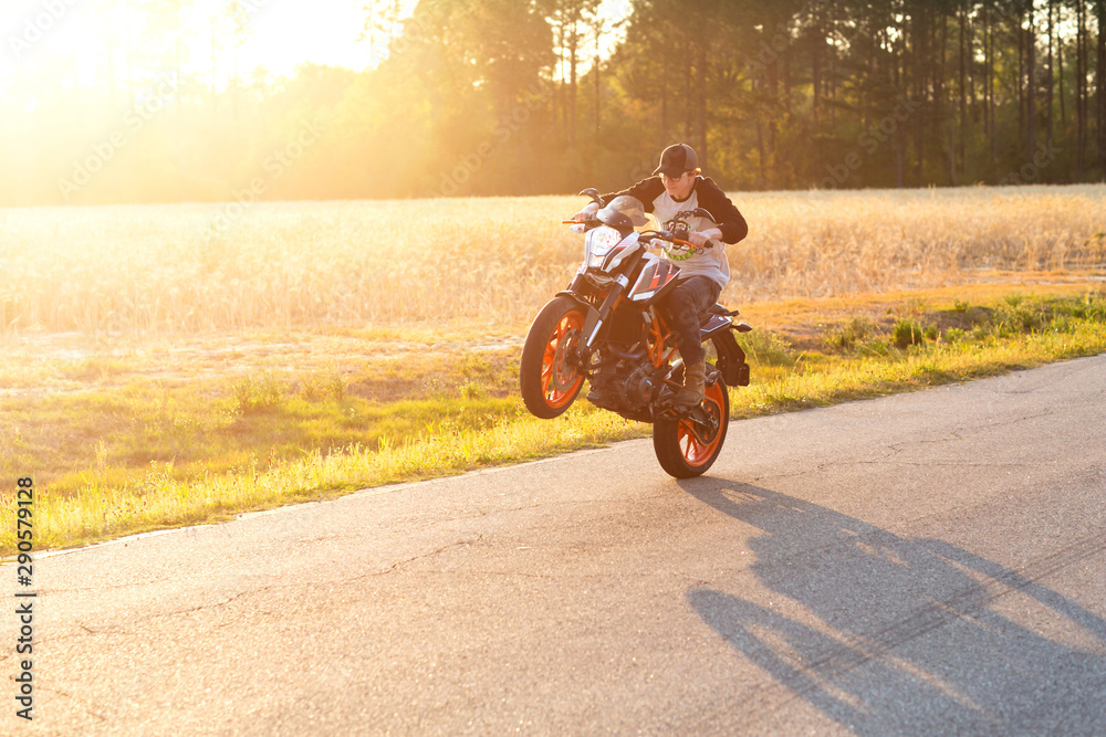 Teenage boy on a dirtbike motorcycle doing a wheelie at sunset - obrazy, fototapety, plakaty 