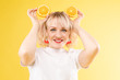 © Вячеслав Косько - Cropped view of sunny blonde in white shirt looking at camera while posing with fruits on yellow isolated background. Happy girl keeping oranges and smiling. Concept of happiness and summer.
