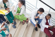 © Алексей Доненко - Doctors are sitting on the steps of the hospital. A group of young people of different gender, mixed race, in medical clothes, with phonendoscopes. Use smartphone, study medical records, study x-rays