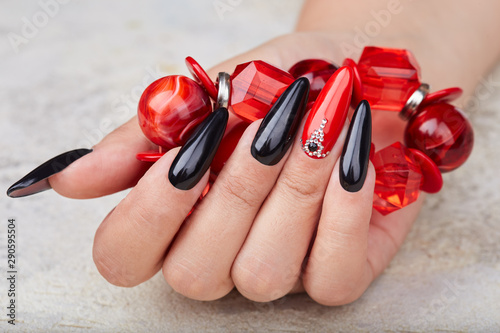 Fotomural Hand with long artificial manicured nails colored with black and red nail polish
