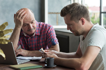 Elderly father and his adult son counting money. Have troubles with taxes and debts