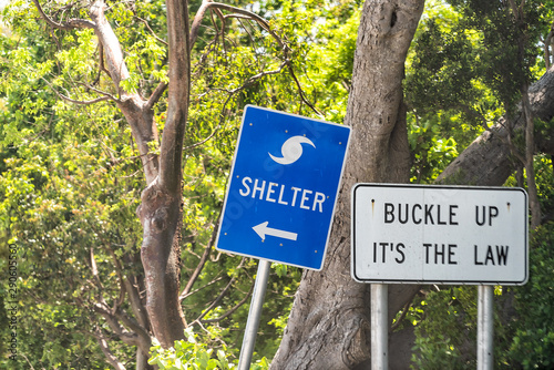 Hurricane evacuation shelter blue sign on road and seat belt buckle up it\'s the law text with arrow direction in Naples, Florida coast during day