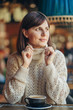 © igishevamaria - Beautiful young woman in warm sweater in the cafe near the window with coffee. Cozy autumn or winter morning.