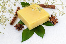 Yellow Handmade Soap Bar On A Green Leaves Over A White Terry Cotton Towel. Natural Toiletries And Hygiene Products With Herbs And Essential Oils.