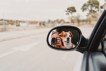 Wall Mural - young woman taking a picture with camera on rear mirror of her cute small jack russell dog watching by the window. Ready to travel. Traveling with pets concept