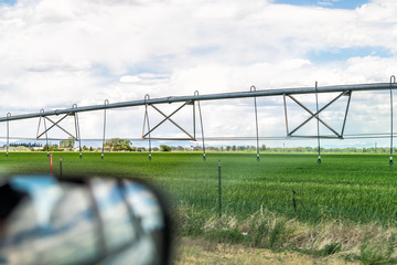 Highway South County Road 100 in Colorado with rural countryside in Monte Vista view of rear view side mirror and modern watering farm tool